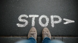 Voeten in wandelschoenen staan voor het woord 'STOP' geschreven in wit krijt op asfalt, symboliseert het stellen van persoonlijke grenzen